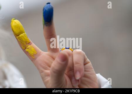 18. September 2022, Hessen, Frankfurt/Main: Eine Frau hält sich bei einer Demonstration zur Unterstützung der Ukraine am Goetheplatz zwei Finger in den Farben der Ukraine hoch und malt ukrainische Flaggen auf die Gesichter der Menschen. Es ist eine Gegendemonstration zu einer pro-russischen Demonstration auf dem Opernplatz. Foto: Sebastian Gollnow/dpa Stockfoto