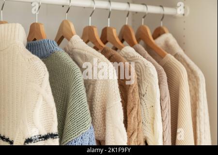 Warmer Winterpullover aus beigefarbener Wolle und Strickmode, die im Kleiderschrank hängen Stockfoto
