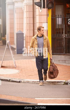 Weiter. Ganzkörperaufnahme eines modischen Mannes, der eine Straße in der Stadt überquert. Stockfoto