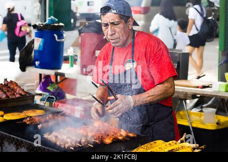 Ein hispanischer Mann, der Straßenfleisch in seinem Speisestand gegrillt, ist ein Verkäufer auf der Avenue Fair 18. in Brooklyn Stockfoto