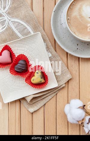 Stimmungsvolle Kaffeepause draußen. Tasse Cappuccino und Pralinen in Herzform. Romantisches Date, Valentinstag. Stockfoto