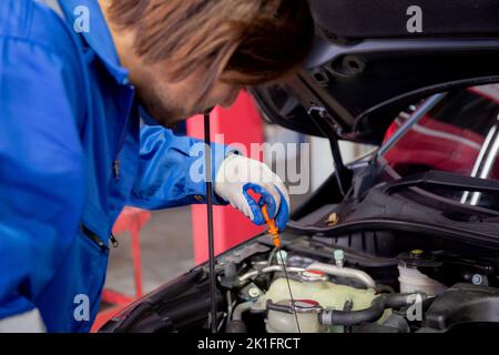 Hände des Arbeiters ist Mann, der Ölmessstab hält, der den Ölstand im Motor des Autos in der Garage überprüft, Mechaniker untersucht und Automobildiagnostik für fix und Stockfoto