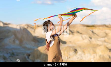 Ein Mädchen von 8-9 Jahren bringt einen Drachen in den Himmel. Stockfoto