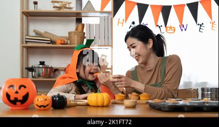 Mutter und ihre Tochter haben Spaß zu Hause. Glückliche Familie bereitet sich auf Halloween vor. Mama und Kind kochen festliche Gerichte in der Küche. Stockfoto