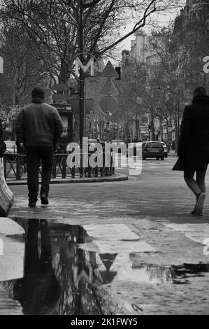 Eine Graustufenaufnahme von Reflexionen in Pfützen, Männer, die durch die Pariser Metro, Frankreich, laufen Stockfoto