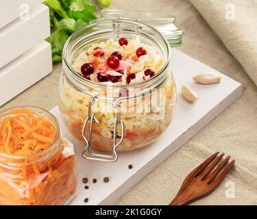 Probiotische Lebensmittel. Eingelegtes oder fermentiertes Gemüse. Koreanische Karotte und Sauerkraut in Gläsern auf einem weißen Brett auf einem Küchentisch. Lebensmittel zu Hause konservieren Stockfoto