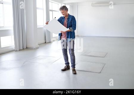 Diese Zimmer werden toll aussehen. Ein reifer Mann, der in einem leeren Raum steht und Baupläne ansieht. Stockfoto