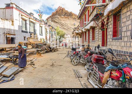 Eine Seitenstraße in der Stadt Gyantse, Präfektur Shigatse, Tibet China mit einer Dzong-Festung im Hintergrund und einer Frau, die unterwegs arbeitet Stockfoto
