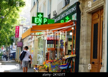 Mann in Fitnesskleidung, der am Obst- und Gemüsemarkt und der Apotheke vorbeigeht, Straßenszene, Alesia, 14. Arrondissement, Paris, Frankreich. Stockfoto