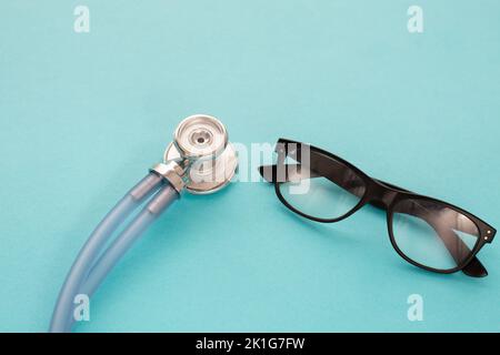 Medizinisches blu Stethoskop und schwarze Brillen auf blu-Hintergrund. Einfach minimalistisches Design mit Medizingeräten Doctor Stethoskop und klassischer Brille Stockfoto