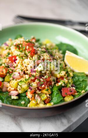 Tabbouleh-Salat mit Bulgur, Tomaten, Petersilie, grüner Zwiebel und Minze auf dem Teller auf dem Tisch aus grauem Stein. Traditionelles mittelöstliches oder arabisches Gericht. Selektiv Stockfoto
