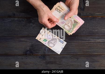 Eine ältere Frau zählt ihr Geld auf einem Holztisch Stockfoto