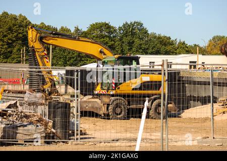 Orangefarbener Straßenkran auf einer Schotterbaustelle mit blauem Himmel und grünen Bäumen im Hintergrund Stockfoto