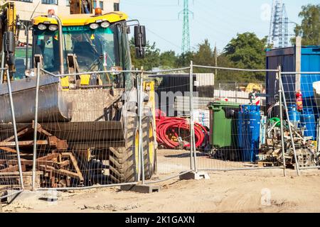 Gelber Straßenkran auf einer Schotterbaustelle mit blauem Himmel und grünen Bäumen im Hintergrund Stockfoto