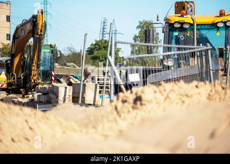 Gelber Straßenkran auf einer Schotterbaustelle mit blauem Himmel und grünen Bäumen im Hintergrund Stockfoto