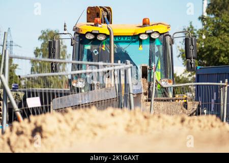 Gelber Straßenkran auf einer Schotterbaustelle mit blauem Himmel und grünen Bäumen im Hintergrund Stockfoto