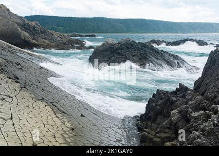 Ufer in natürlichem Lava-Damm, Meeresbrandung zwischen Küstenfelsen mit Blick auf die ferne Küste Stockfoto