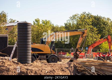 Gelber Straßenkran auf einer Schotterbaustelle mit blauem Himmel und grünen Bäumen im Hintergrund Stockfoto