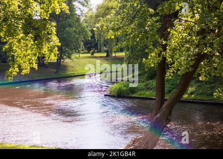 Eine Landschaft mit einem Kanal, grünen Bäumen und einem Regenbogen darüber Stockfoto