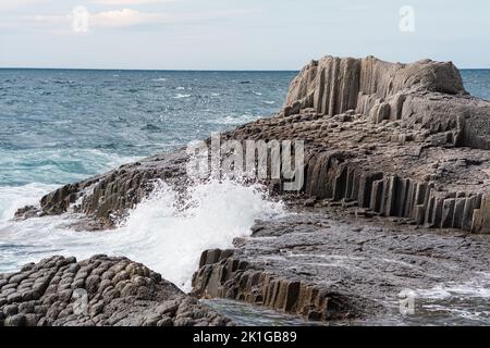 Felsen, die durch säulenförmigen Basalt zwischen der Meeresbrandung am Kap Stolbchaty auf der Insel Kunashir gebildet werden Stockfoto