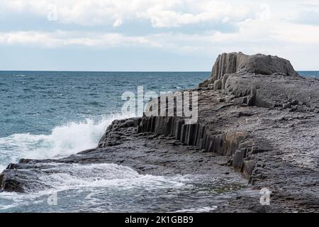 Felsen, die durch säulenförmigen Basalt zwischen der Meeresbrandung am Kap Stolbchaty auf der Insel Kunashir gebildet werden Stockfoto