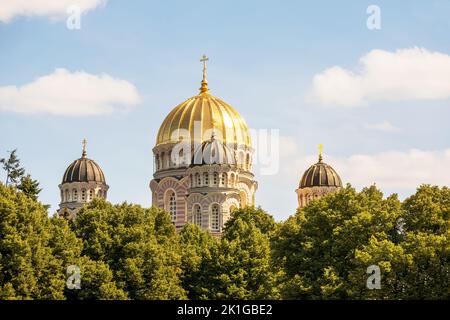 Eine Kirche mit einer gelben Mauer und einer spitzen goldenen Spitze mitten im Stadtzentrum mit mehreren Fenstern und Bäumen daneben Stockfoto