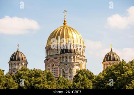 Eine Kirche mit einer gelben Mauer und einer spitzen goldenen Spitze mitten im Stadtzentrum mit mehreren Fenstern und Bäumen daneben Stockfoto