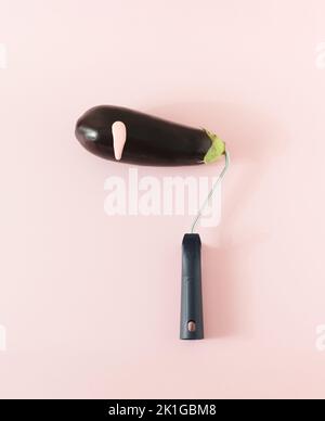 Eine frische Aubergine / Aubergine auf einem Farbrollengriff mit einem Tropfen einer rosa Farbe auf einem rosa Hintergrund montiert. Minimalkonzept. Stockfoto