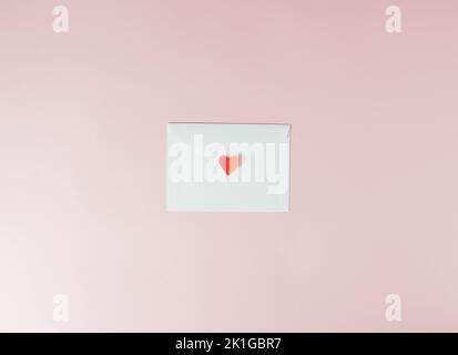 Liebesbrief zum Valentinstag in einem weißen Umschlag auf einem hellrosa Hintergrund, der mit einem roten Herzen versiegelt ist. Minimalkonzept. Stockfoto