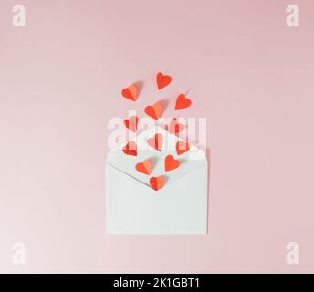 Rote Papierherzen fliegen aus einem weißen Umschlag - Valentinskarte. Minimalkonzept. Stockfoto