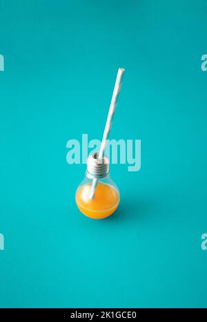 Energy Orange Drink in Glühbirne mit gestreiftem Trinkhalm auf blauem Hintergrund. Stockfoto