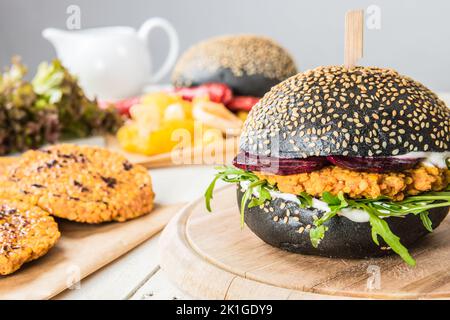 Schwarzer veganer Burger mit roten Linsenpasteten und Rote-Bete-Scheiben und frischer Rucola. Schwarzes Brötchen und veganer Hamburger. Rote Linsen voller pflanzlicher Proteine. Stockfoto