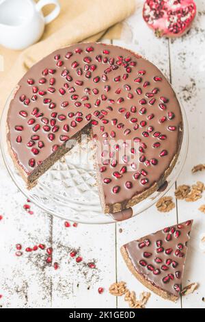 Veganer Mohnkuchen mit Walnüssen und hausgemachter Weißdornmarmelade. Köstliche hausgemachte Kuchen mit veganer Schokolade bedeckt. Granatapfel auf dem Dessert. Stockfoto