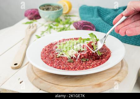 Veganes Essen, Risotto mit Rote Beete, verziert mit veganem Käse, Kürbiskernen und frischer Rucola. Auf dem weißen rustikalen Tisch. Frisches Bio-Gemüse. Stockfoto