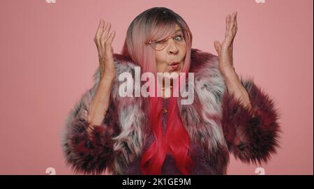 Warum. Aufrichtige irritierte ältere Frau, die in empörtem Ausdruck die Hände aufhob und nach dem Grund des Scheiterns fragte und Ungläubigkeit zeigte, die durch Probleme gereizt wurde. Ältere verworrene Großmutter auf rosa Hintergrund Stockfoto