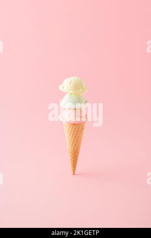 Eiscreme mit drei Kugeln in einem Kegel, vertikal auf rosa Hintergrund platziert. Minimales Sommerkonzept. Stockfoto