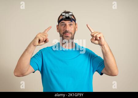 Latino bärtiger Mann mit einer Glühbirne auf dem Kopf, die mit den Fingern darauf zeigt, Erkundungen im Freien und Abenteueraktivitäten, isoliert beige Stockfoto