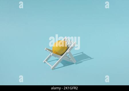 Frische Zitrone auf einem Liegestuhl mit blauem Hintergrund. Farbenfrohes, kreatives Sommerfood-Konzept. Stockfoto
