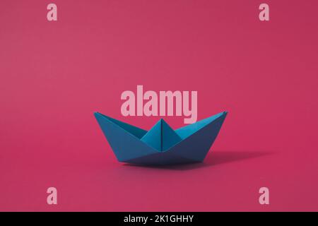 Blaues Origami-Papier Boot auf rosa Hintergrund. Minimalkonzept. Stockfoto