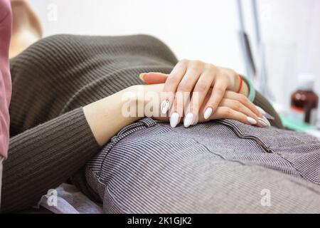 Eine Patientin auf dem Untersuchungstisch im Ultraschalldiagnoseschrank. Eine Frau liegt auf einer Couch mit gefalteten Händen auf dem Bauch und wartet auf ein besonderes Stockfoto