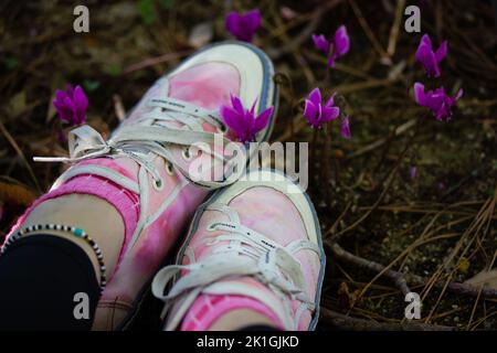 Madrid, Spanien. 6. September 2022 stilvolles Mädchen in rosa Sneakers sitzt zwischen lila violetten Cyclamen hederifolium Blumen am Waldrand, Garten, Park. Stockfoto