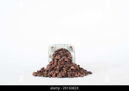 Haufen von natürlichen rohen Kakaospitzen aus dem Glas gegossen, isoliert auf weißem Hintergrund. Stockfoto