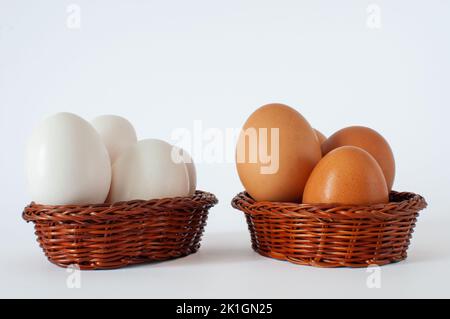 Braune und weiße Hühnereier in braunen Mini-Körben, isoliert auf weißem Hintergrund. Legen Sie nicht alle Ihre Eier in einem Korb Idee Konzept. Stockfoto