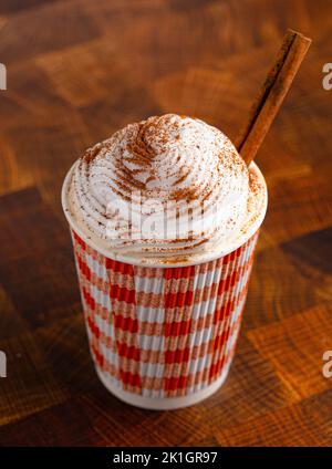 Ein Kürbis Gewürz Latte gekrönt mit Schlagsahne in einem Einweg-Becher auf einem Holztisch Stockfoto