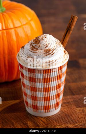 Ein Kürbis Gewürz Latte gekrönt mit Schlagsahne in einem Einweg-Becher auf einem Holztisch Stockfoto