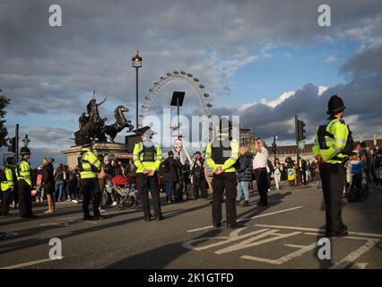 London, Großbritannien. 18. September 2022. Polizeibeamte stehen auf der Westminster Bridge in der Nähe der Westminster Hall und Passanten stehen Schlange, um am Sarg im Parlament von Königin Elizabeth II Abschied zu nehmen. Die britische Königin Elizabeth II. Starb am 8. September 2022 im Alter von 96 Jahren. Der Sarg mit der Königin wird vier Tage lang im Palace of Westminster (Parlament) angelegt. Für den 19. September ist eine staatliche Zeremonie in Westminster Abbey mit rund 2000 Gästen und die Beerdigung im Windsor Castle bei London geplant. Quelle: Christian Charisius/dpa/Alamy Live News Stockfoto