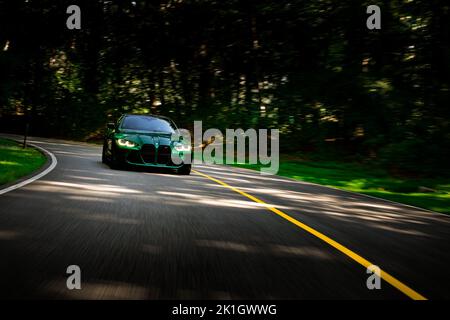 Rollende Aufnahme des BMW M4 Performance auf asphaltierter Straße mit verwischten Bäumen im Hintergrund Stockfoto
