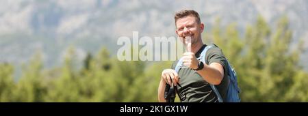 Lächelnder Mann mit skandinavischen Wanderstöcken auf dem Hintergrund des Berges Stockfoto