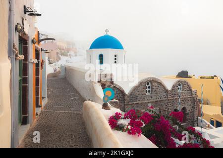 Ein nebliger, nebliger Morgen entlang einer ruhigen, malerischen gepflasterten Gasse neben der traditionellen griechischen orthodoxen Kirche Panagia Agion Panton mit blauer Kuppel im CO Stockfoto