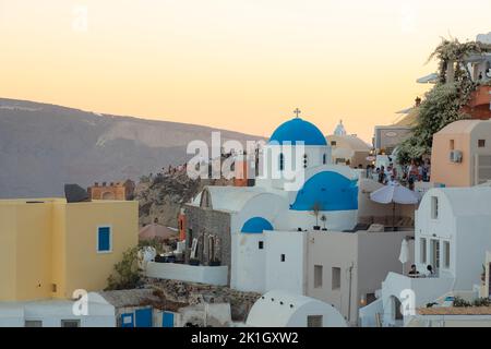 Oia, Griechenland - 11 2022. September: Sonnenuntergangsansicht der traditionellen weißen Waschhäuser und der blauen Kuppelkirche Panagia Agion Panton bei der beliebten Strandtour Stockfoto